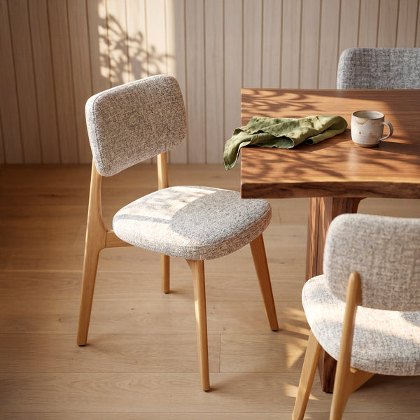 COLAMY HALO natural oak upholstered dining chair with textured mixed-weave fabric beside a wooden dining table