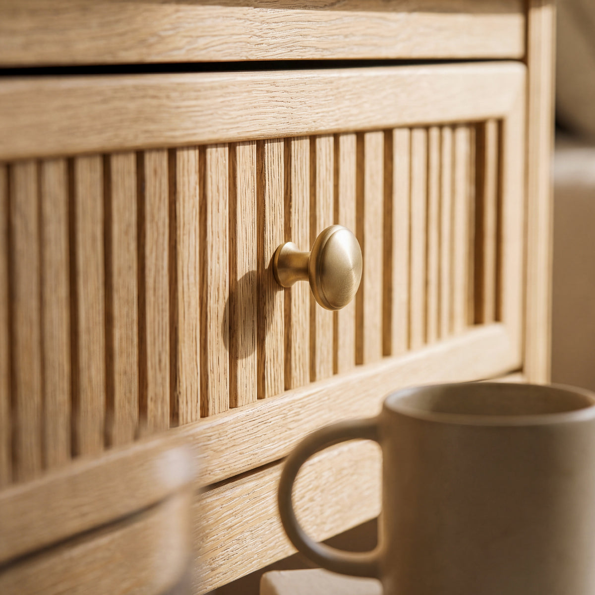 fluted drawer side table close up with a reeded oak drawer front brass round knob and a ceramic mug
